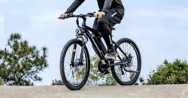Un cycliste franchit une crête de terre sur le VTT électrique Touroll U1, ciel dégagé en arrière-plan
